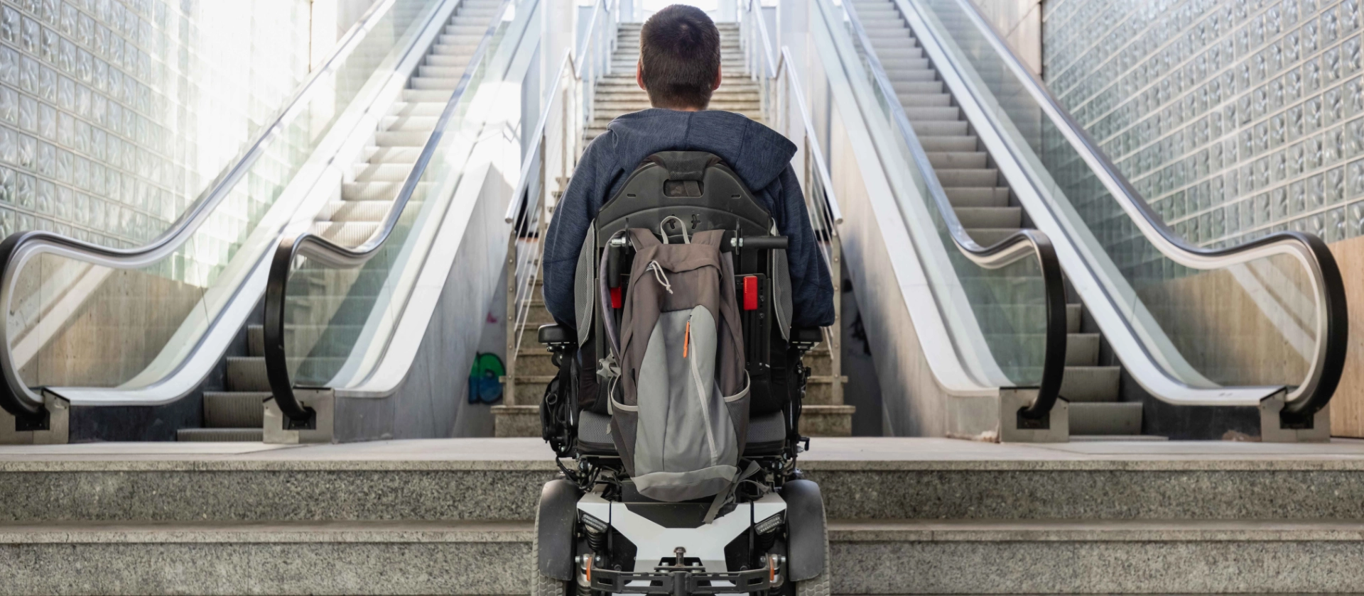 Mann im Rollstuhl vor Treppe und Rolltreppe Barrierefreiheit