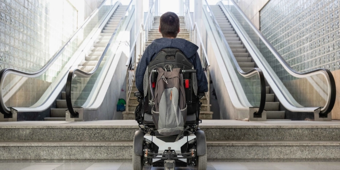 Mann im Rollstuhl vor Treppe und Rolltreppe Barrierefreiheit