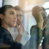 Shot of a group of colleagues brainstorming together on a glass wall in an office.
